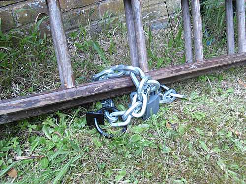 Ancrage au sol, chaîne et cadenas sur échelle en bois.
